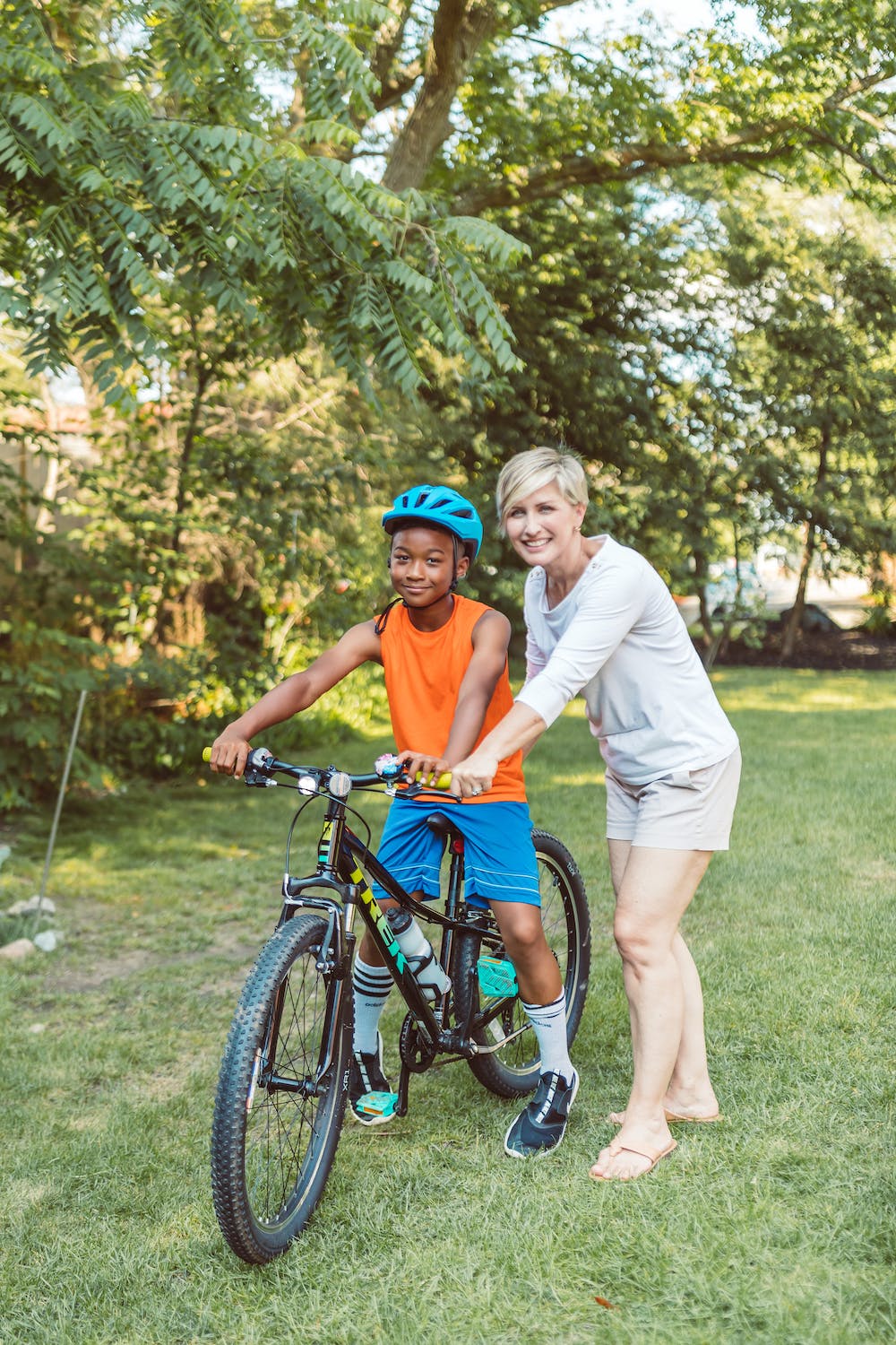 child on bike withhelmet being helped by woman