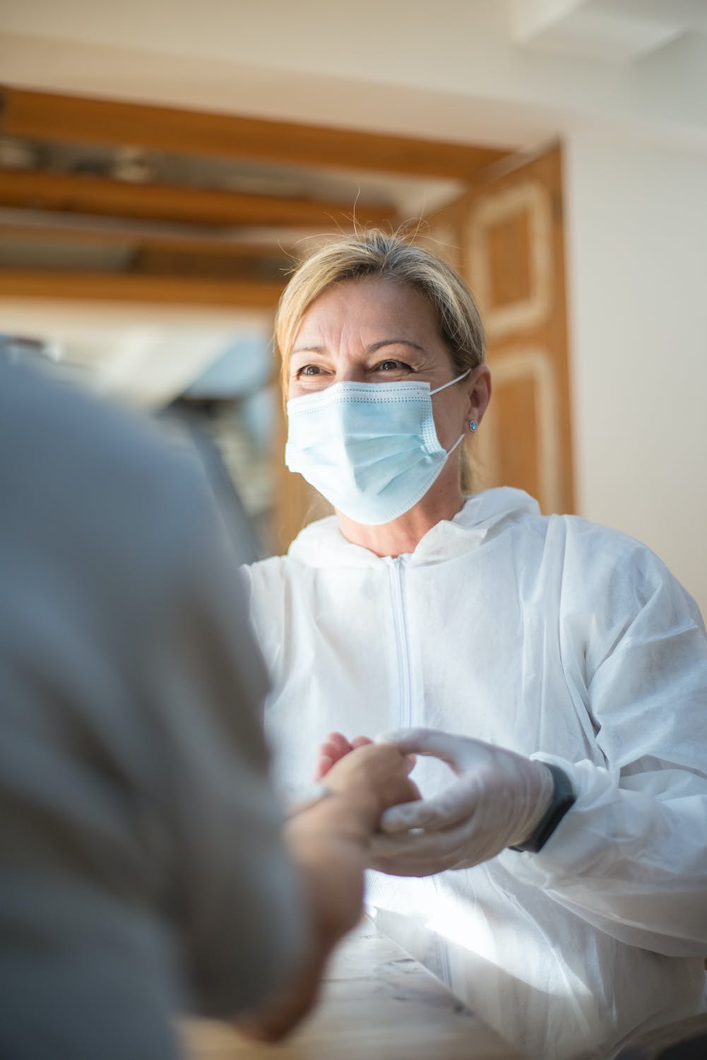 masked nurse smiling and holding a persons hand